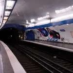 The platform of Jussieu metro station in Paris: empty blue seats under a white tiled vault, the track disappearing into the tunnel on the left