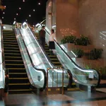 Two escalators and a staircase side by side in a shopping arcade at night, one woman riding up alone